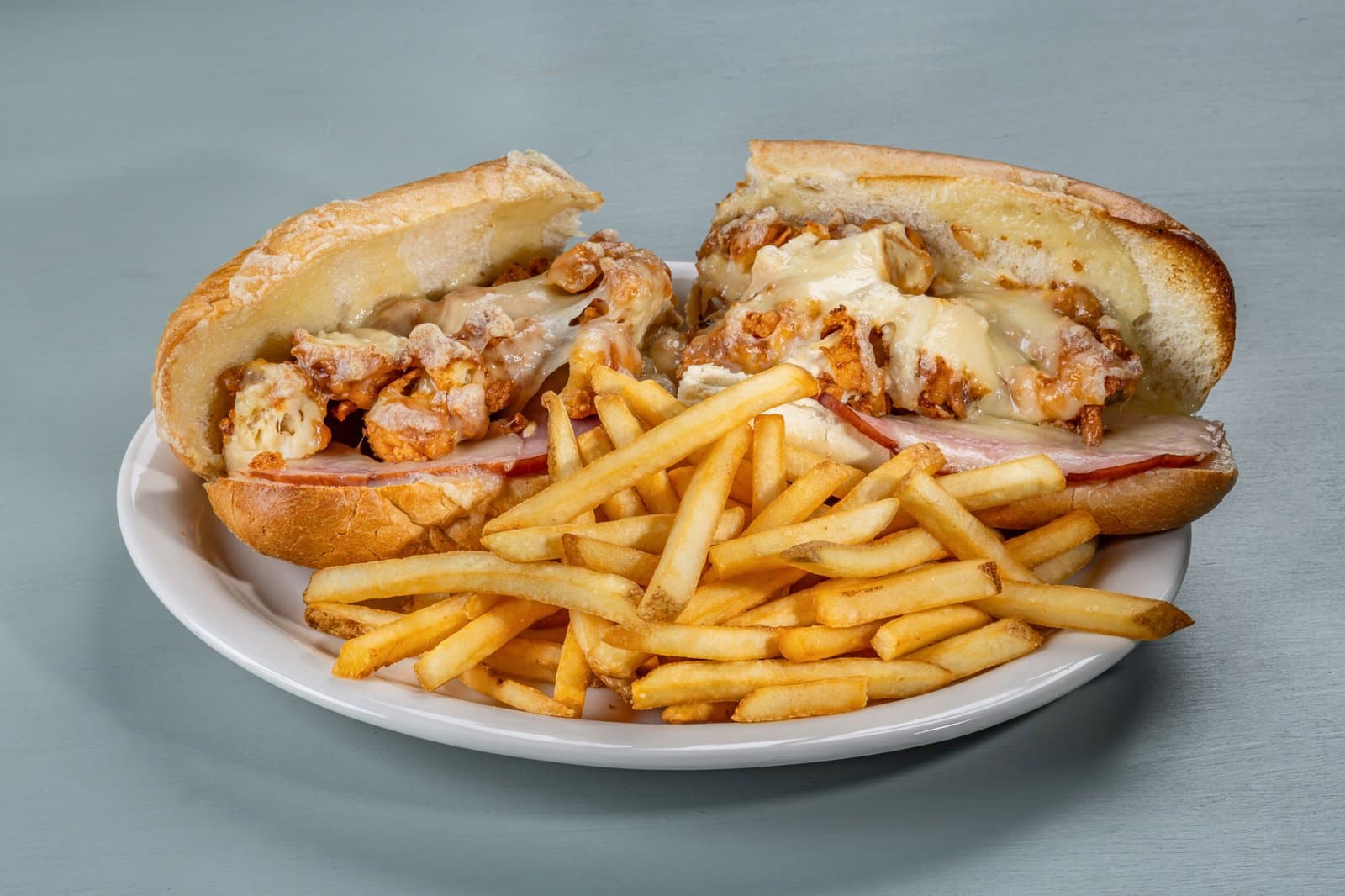 Crispy chicken sub with ham and melted cheese, served with fries