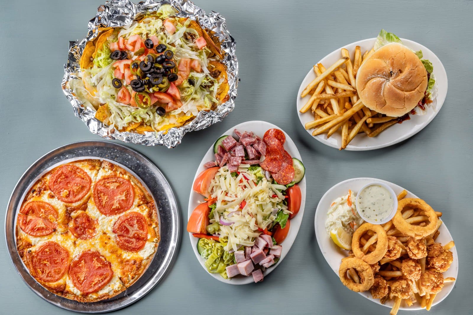Overhead dinner spread with nachos, pizza, salad, burger, and fried platter