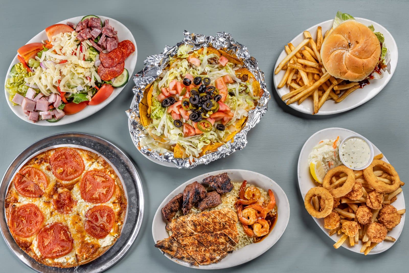 Family feast spread of salad, nachos, burger, pizza, and fried seafood