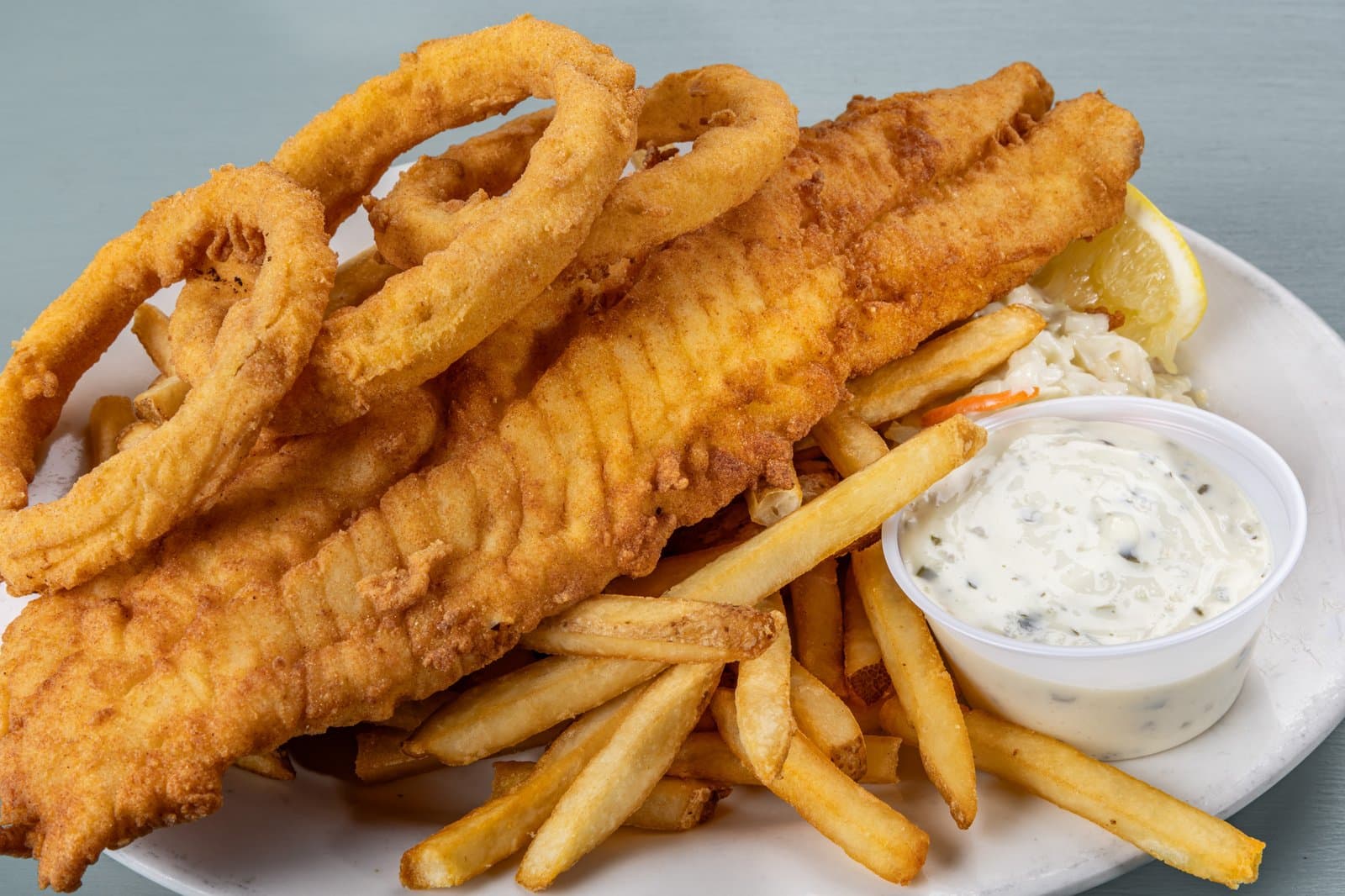 Fried fish and chips with onion rings, coleslaw, and tartar sauce