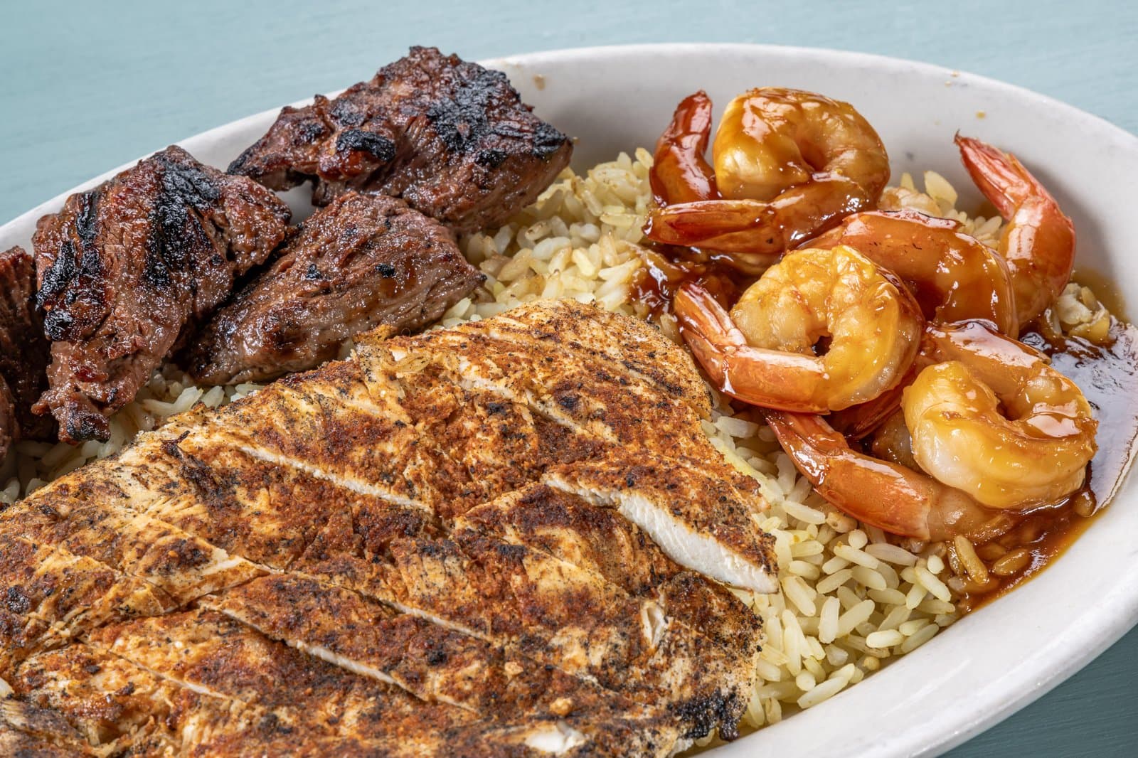 Close-up of steak tips, blackened chicken, and teriyaki shrimp over rice