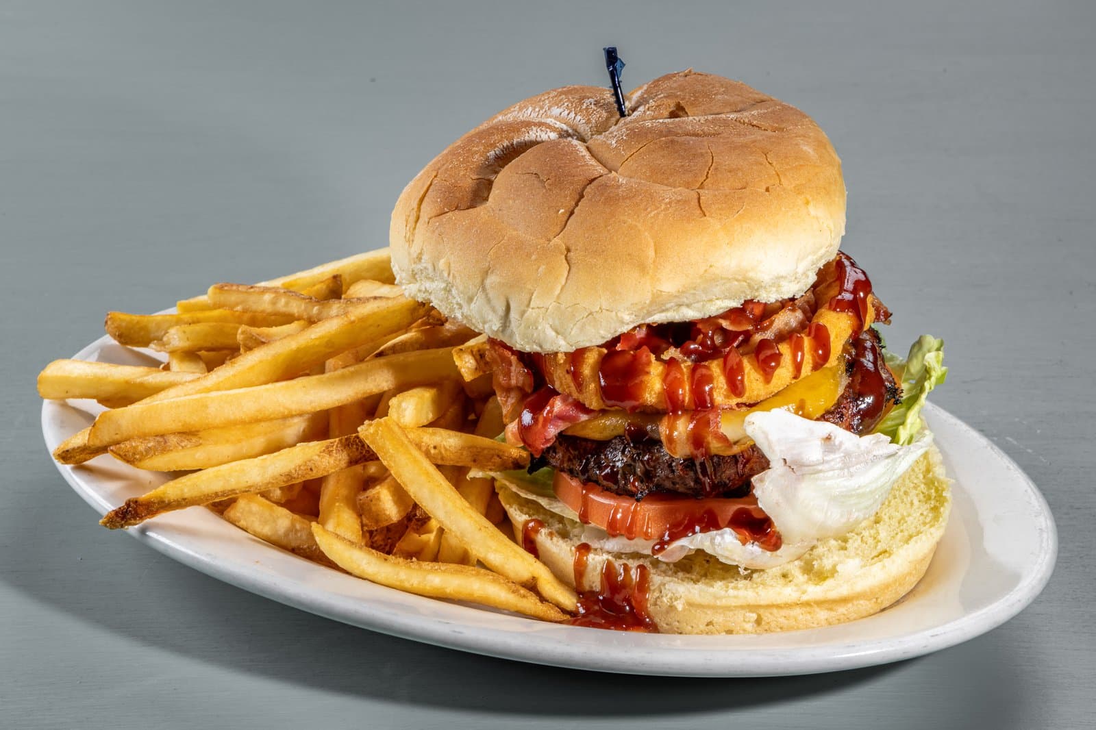 The Smoke House Burger stacked with bacon, onion rings, and BBQ sauce, with fries