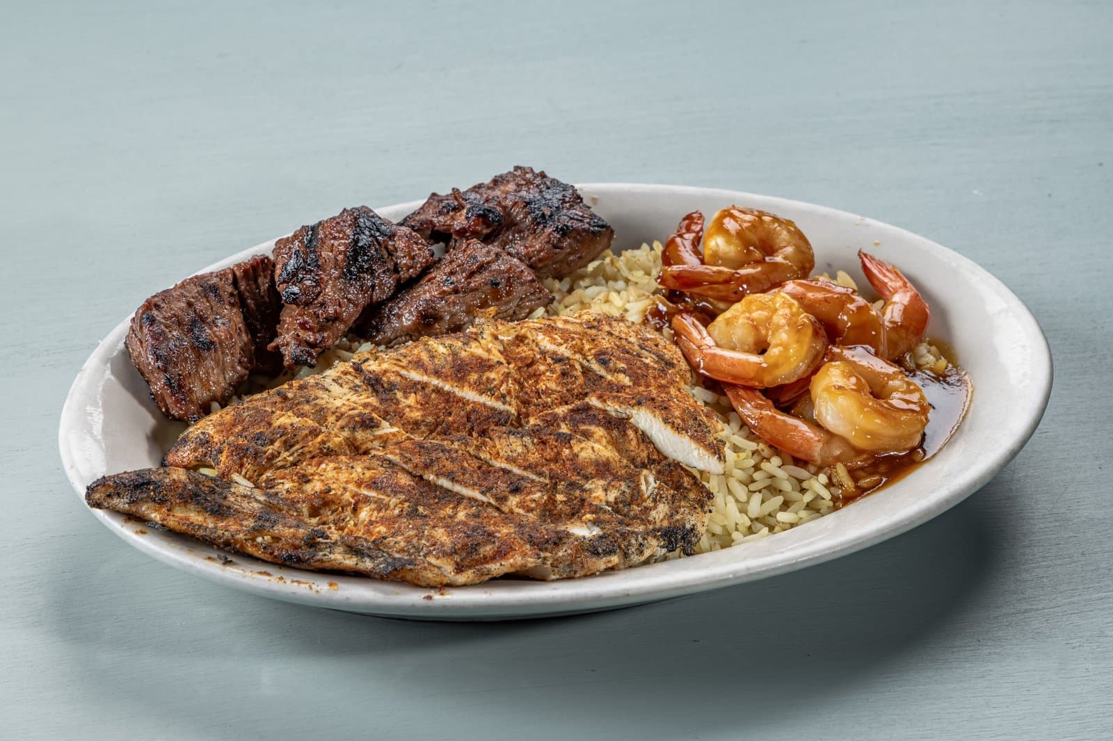 Grilled steak tips, blackened chicken, and teriyaki shrimp over rice