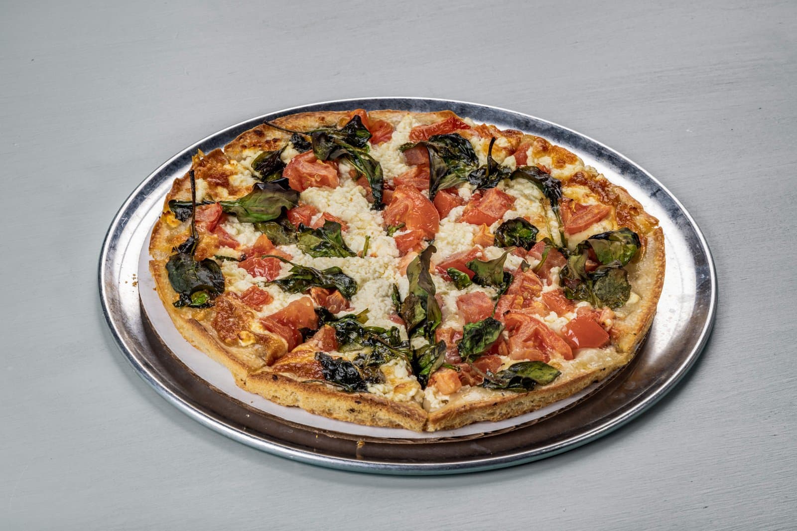 Thin-crust pizza with tomato, crispy basil, and feta
