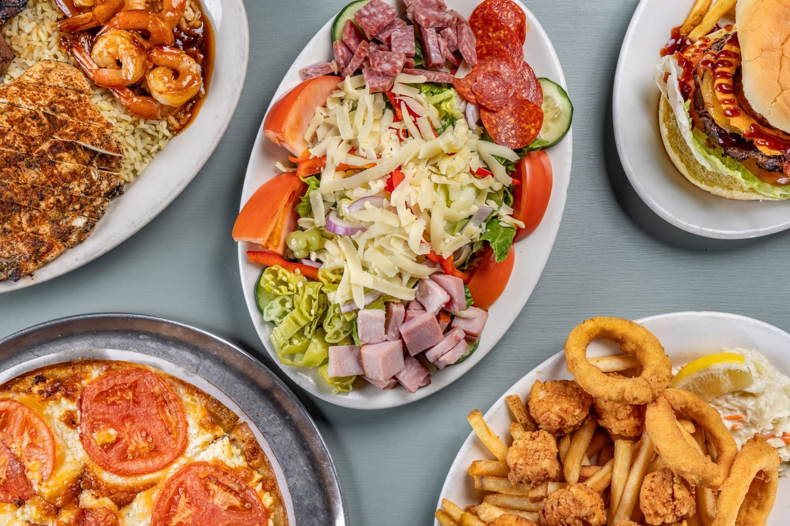 Overhead spread of salad, pizza, burger, and fried seafood plates